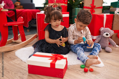 Brother and sister playing with toys sitting on floor by christmas gifts at home