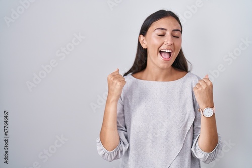 Young hispanic woman standing over white background celebrating surprised and amazed for success with arms raised and eyes closed. winner concept.