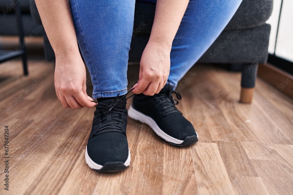 Young beautiful plus size woman tying shoe at home Young beautiful plus size woman tying shoe at home