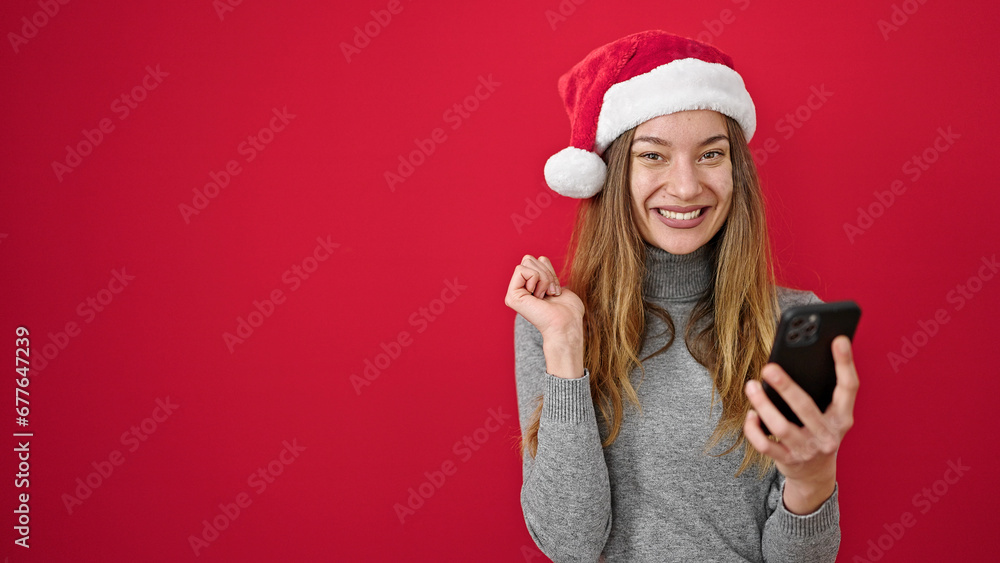 Young caucasian woman wearing christmas hat using smartphone over isolated red background Young caucasian woman wearing christmas hat using smartphone over isolated red background