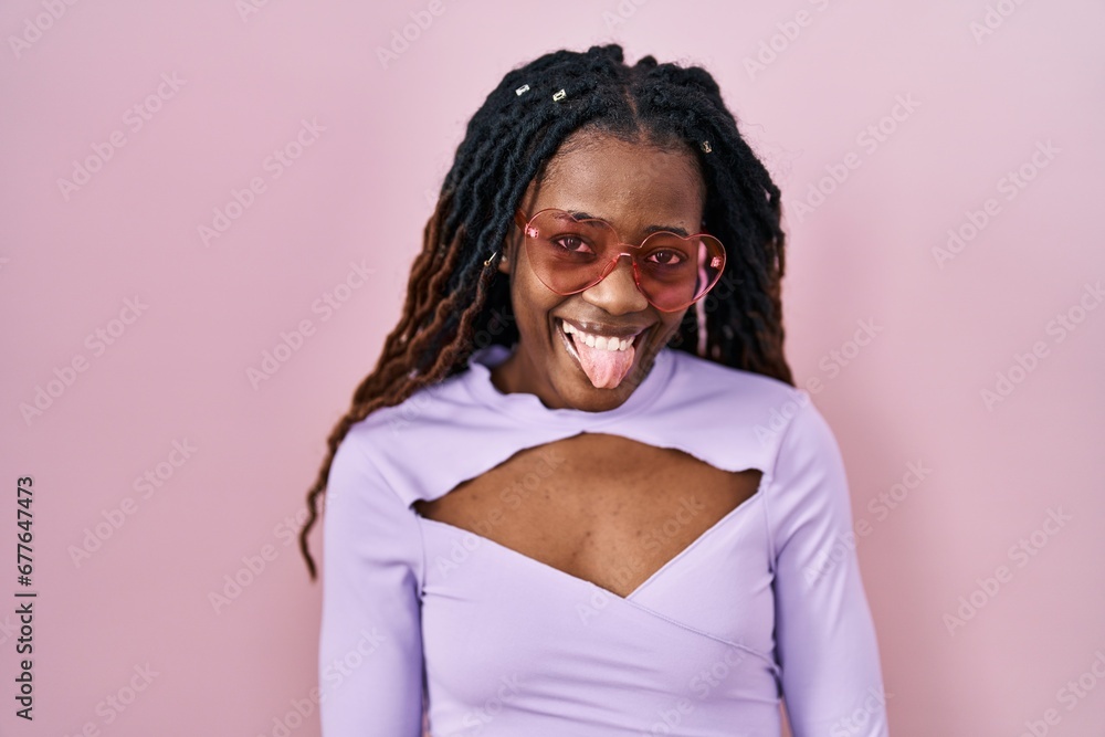 African woman with braided hair standing over pink background sticking tongue out happy with funny expression. emotion concept. African woman with braided hair standing over pink background sticking tongue out happy with funny expression. emotion concept.