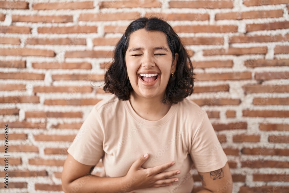Young hispanic woman standing over bricks wall smiling and laughing hard out loud because funny crazy joke with hands on body. Young hispanic woman standing over bricks wall smiling and laughing hard out loud because funny crazy joke with hands on body.