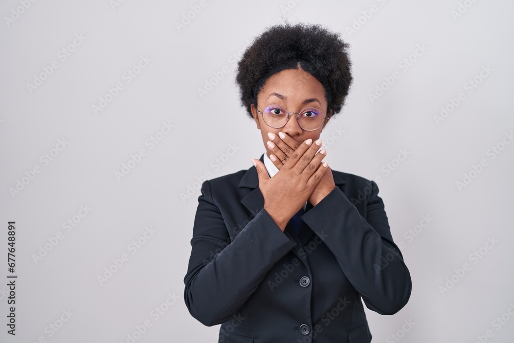 Beautiful african woman with curly hair wearing business jacket and glasses shocked covering mouth with hands for mistake. secret concept. Beautiful african woman with curly hair wearing business jacket and glasses shocked covering mouth with hands for mistake. secret concept.