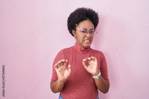 Принти на полотні Beautiful african woman with curly hair standing over pink background disgusted expression, displeased and fearful doing disgust face because aversion reaction