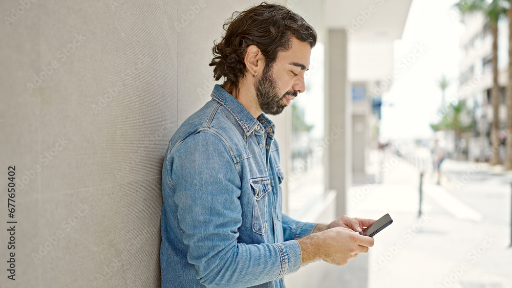 Fototapeta premium Young hispanic man using smartphone with serious expression at street