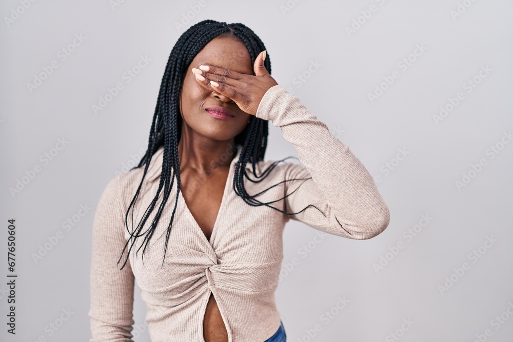 African woman with braids standing over white background covering eyes with hand, looking serious and sad. sightless, hiding and rejection concept African woman with braids standing over white background covering eyes with hand, looking serious and sad. sightless, hiding and rejection concept