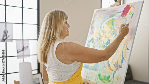 Beautiful middle age blonde woman artist seriously concentrating on drawing in her indoor art studio