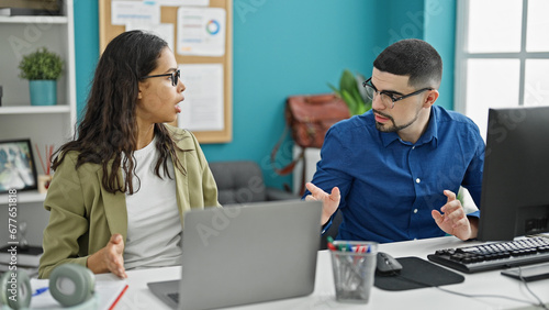 Two office workers, a man and woman, sitting at a table, entangled in a heated argument at their workplace