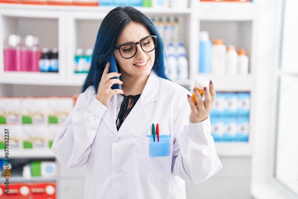 Young caucasian woman pharmacist holding pills bottle talking on smartphone at pharmacy