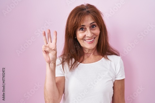 Wallpaper Mural Middle age woman standing over pink background showing and pointing up with fingers number three while smiling confident and happy. Torontodigital.ca