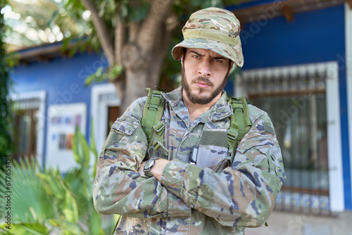 Young hispanic man wearing camouflage army uniform outdoors skeptic and nervous, disapproving expression on face with crossed arms. negative person.