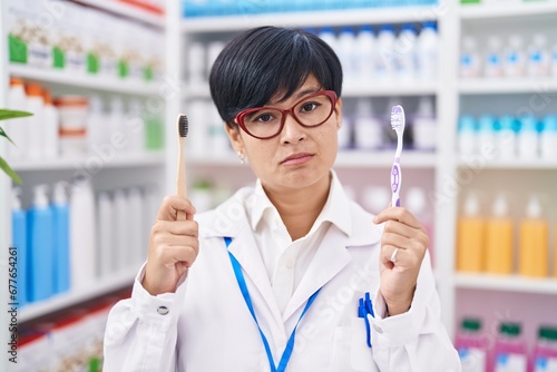 Young asian woman with short hair doing toothbrush comparative at pharmacy relaxed with serious expression on face. simple and natural looking at the camera.
