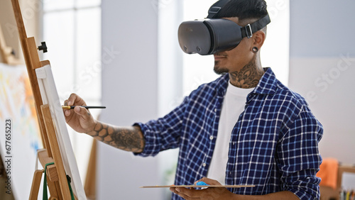 Talented young latin man artist engrossed in painting class, drawing art masterpiece using futuristic virtual reality glasses indoors at studio