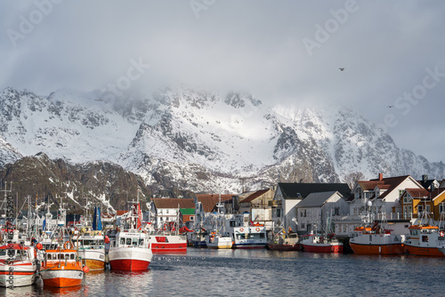 Fishing village close to snow capped mountains. Photograph of Henningsvær harbor in the Lofoten Islands in Norway (ID: 677655290)