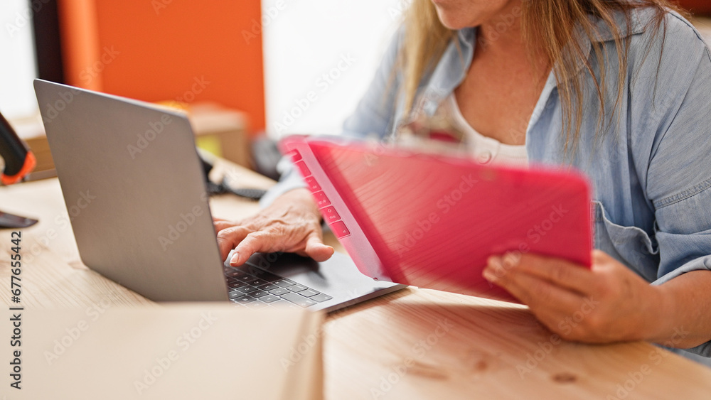 Fototapeta premium Middle age hispanic woman ecommerce business worker using laptop reading document at office