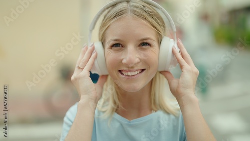 Young blonde woman listening to music standing at street