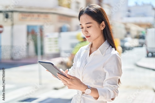 Obraz na plátně Young chinese woman using touchpad with serious expression at street