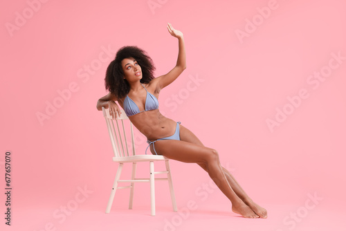 Beautiful woman in stylish bikini posing on chair against pink background
