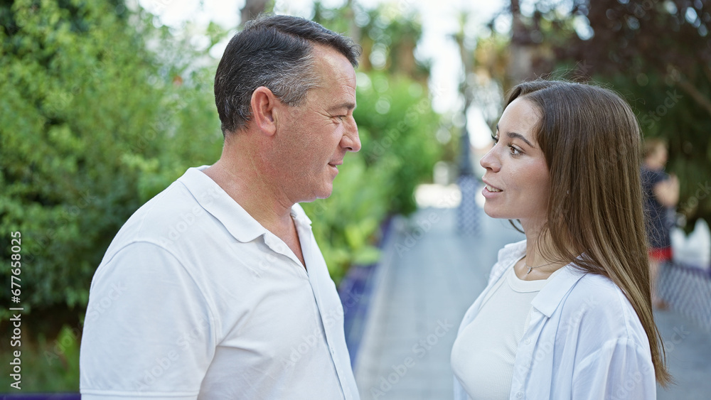 Confident hispanic father and daughter engage in warm conversation, standing together, smiling, radiating positivity in the heart of the sunny park Confident hispanic father and daughter engage in warm conversation, standing together, smiling, radiating positivity in the heart of the sunny park