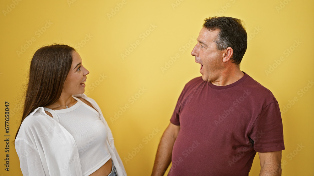 Cool hispanic father and his lovely daughter sharing a surprise, looking amazed over isolated yellow background, showcasing family love and confidence Cool hispanic father and his lovely daughter sharing a surprise, looking amazed over isolated yellow background, showcasing family love and confidence