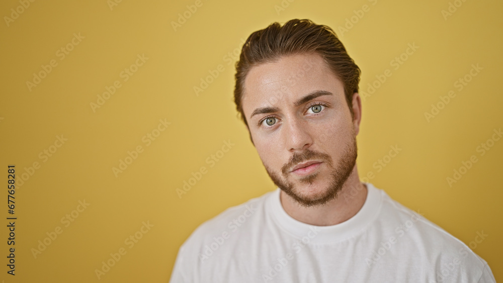 Young hispanic man standing with serious expression over isolated yellow background Young hispanic man standing with serious expression over isolated yellow background