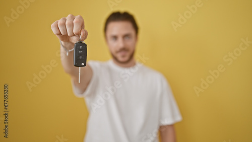 Young hispanic man holding key of new car over isolated yellow background