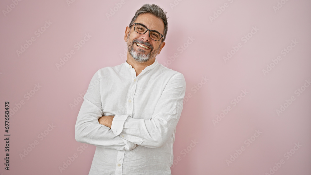 Happy, confident young hispanic man with grey hair and cool glasses, standing relaxed over an isolated pink background, casually crossing arms, flashing a cheery smile. Happy, confident young hispanic man with grey hair and cool glasses, standing relaxed over an isolated pink background, casually crossing arms, flashing a cheery smile.