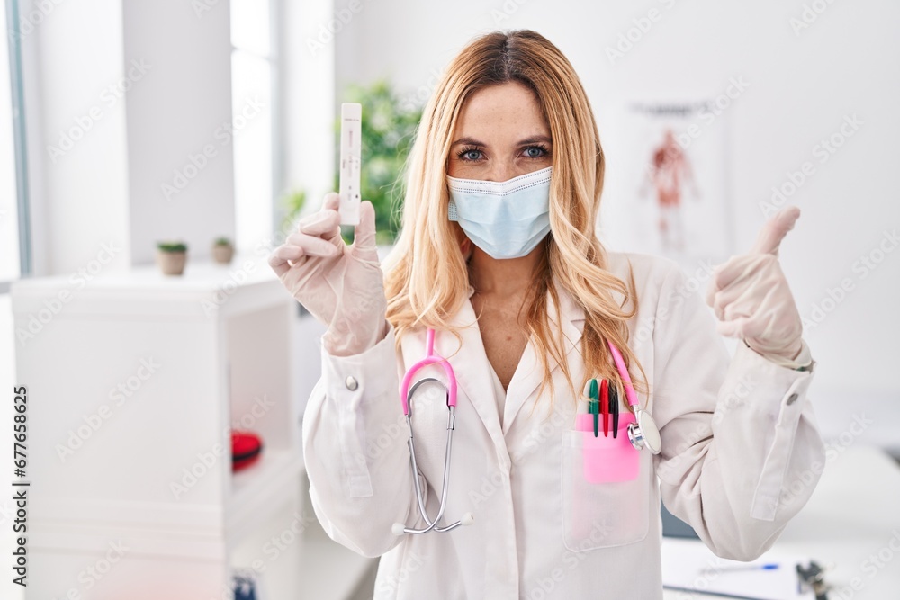 Young caucasian doctor woman holding covid test smiling happy and positive, thumb up doing excellent and approval sign Young caucasian doctor woman holding covid test smiling happy and positive, thumb up doing excellent and approval sign
