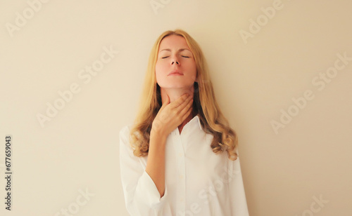 Sick young woman touches her neck with hand while suffering from acute sore in throat flu, she feels bad photo
