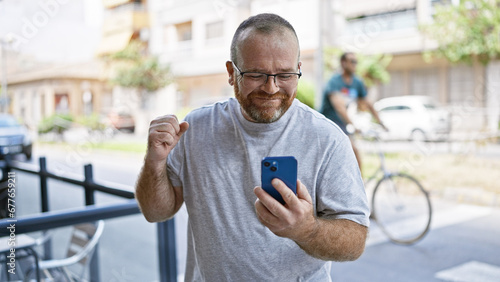 Eureka! cheerful middle-aged caucasian man with beard, firstly celebrating using smartphone on outdoor city street, texting a winning message!