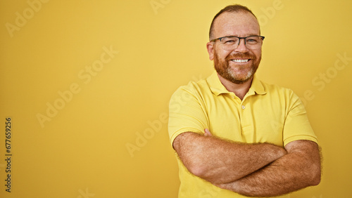 Cheerful handsome middle age caucasian man exuding confidence and joy, standing with a fun laughing expression, his arms crossed against a vibrant yellow isolated background