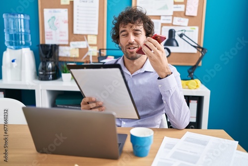 Young hispanic man business worker talking on smartphone reading document at office