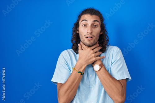 Young hispanic man standing over blue background shouting suffocate because painful strangle. health problem. asphyxiate and suicide concept.