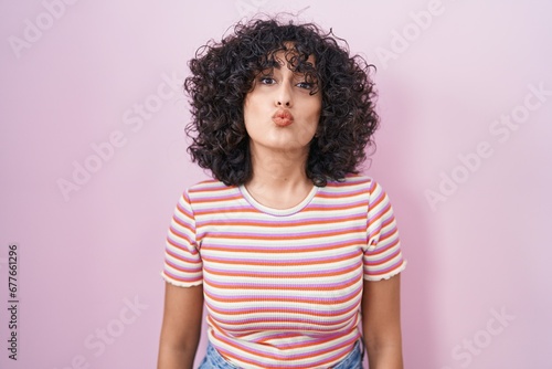 Young middle east woman standing over pink background looking at the camera blowing a kiss on air being lovely and sexy. love expression. © Krakenimages.com
