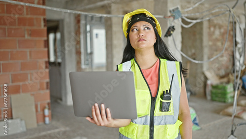 Young chinese woman architect using laptop looking around at construction site