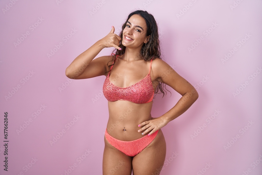 Obraz premium Young hispanic woman wearing lingerie over pink background smiling doing phone gesture with hand and fingers like talking on the telephone. communicating concepts.