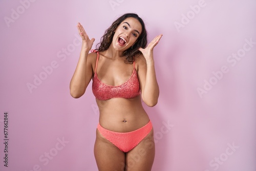 Young hispanic woman wearing lingerie over pink background celebrating crazy and amazed for success with arms raised and open eyes screaming excited. winner concept