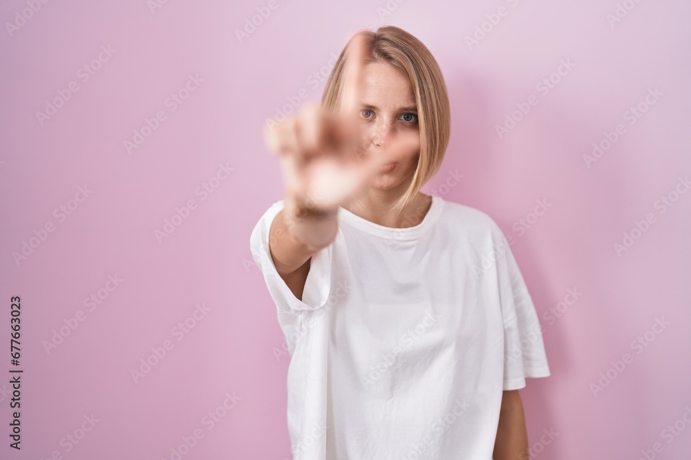 Young caucasian woman standing over pink background pointing with finger up and angry expression, showing no gesture Young caucasian woman standing over pink background pointing with finger up and angry expression, showing no gesture