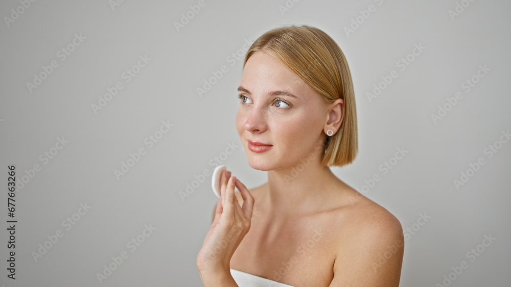Young blonde woman cleaning face with cotton pad over isolated white background Young blonde woman cleaning face with cotton pad over isolated white background