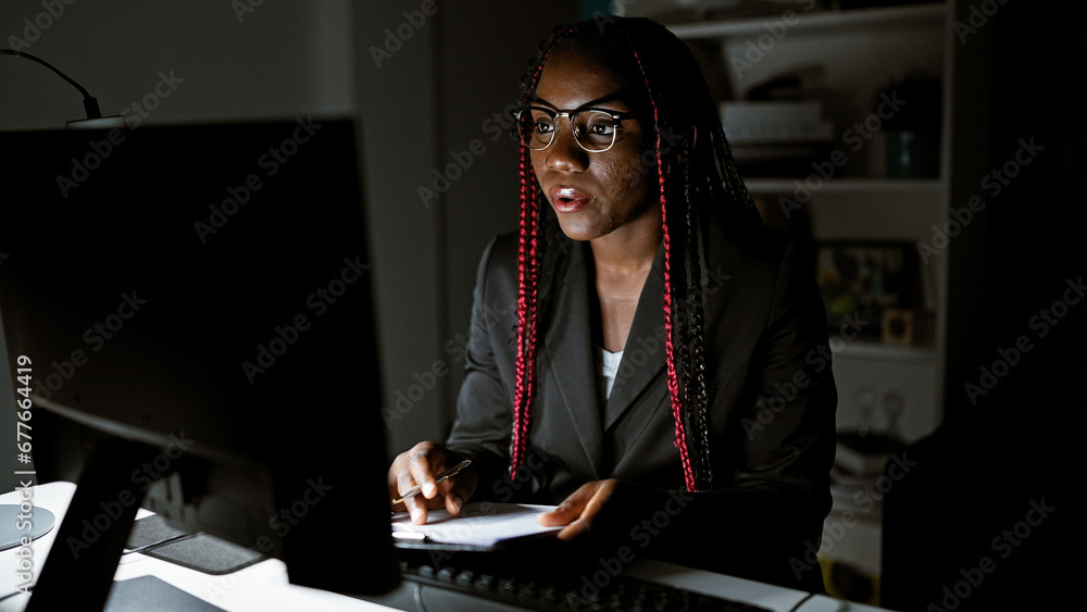 Working night magic, african american business woman rocks it at the office, taking notes and juggling a video call. portraying success she commands the interior room with confidence - obrazy, fototapety, plakaty 