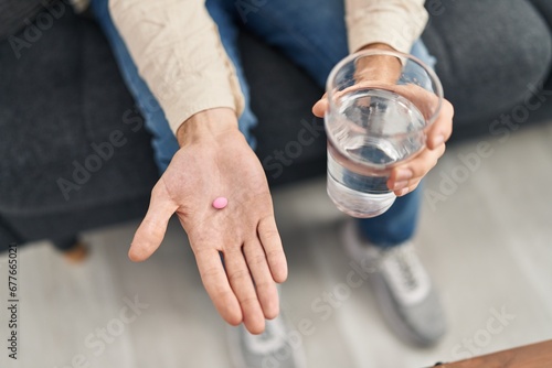 Young caucasian man holding pill and glass of water at psychology clinic