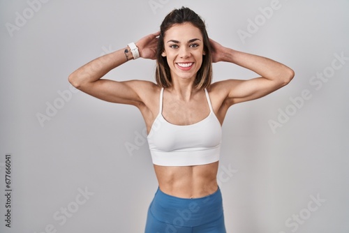 Hispanic woman wearing sportswear over isolated background relaxing and stretching, arms and hands behind head and neck smiling happy photo