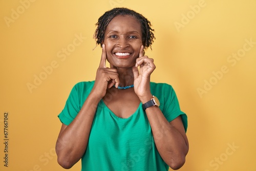 African woman with dreadlocks standing over yellow background smiling with open mouth, fingers pointing and forcing cheerful smile