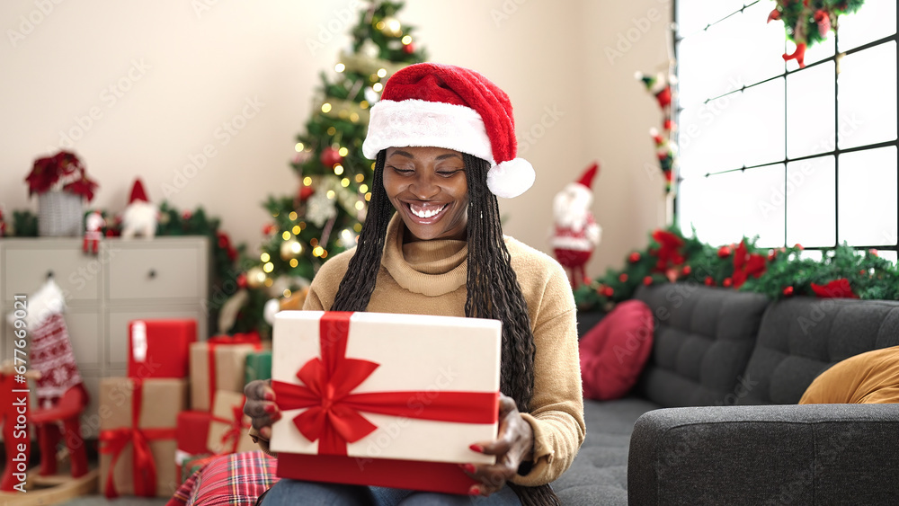 African woman unpacking gift sitting by christmas tree at home African woman unpacking gift sitting by christmas tree at home