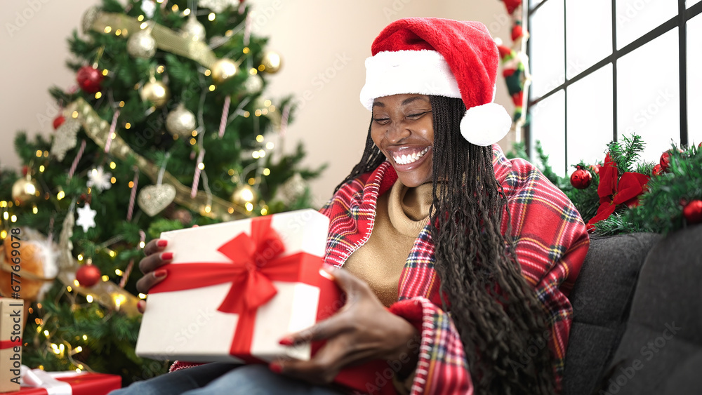 African woman unpacking gift sitting by christmas tree at home African woman unpacking gift sitting by christmas tree at home
