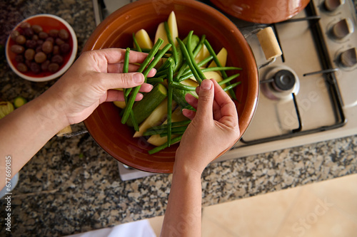 View from above of housewife hands putting fresh organic green beans on the tagine while cooking dinner in the kitchen © Taras Grebinets