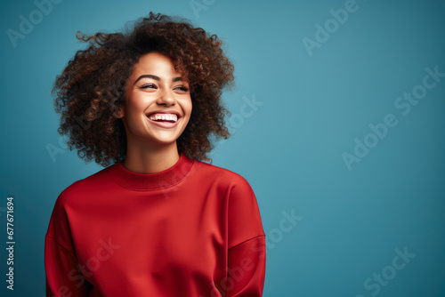 Vibrant Joy: Smiling African American Woman in Red Sweater, Blue Background with copy space © mimagephotos