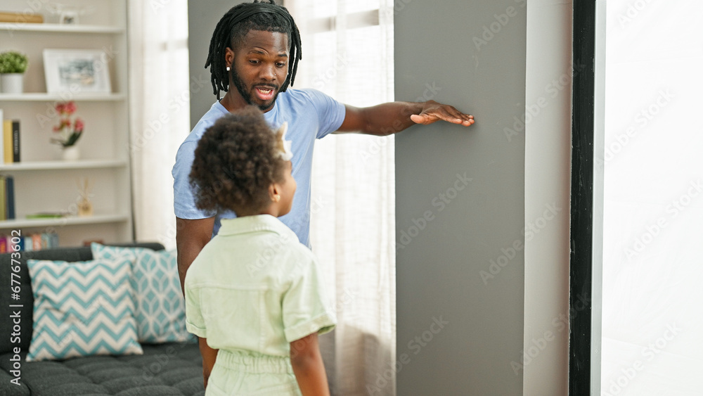 African american father and daughter smiling confident measuring height on wall at home - obrazy, fototapety, plakaty 