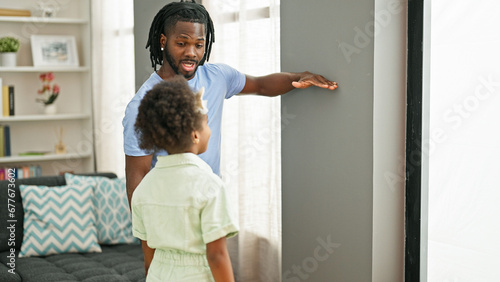 African american father and daughter smiling confident measuring height on wall at home