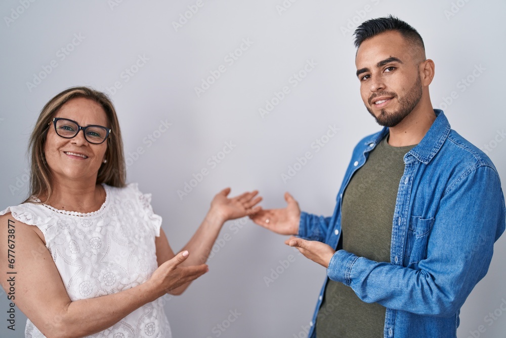Hispanic mother and son standing together inviting to enter smiling natural with open hand Hispanic mother and son standing together inviting to enter smiling natural with open hand